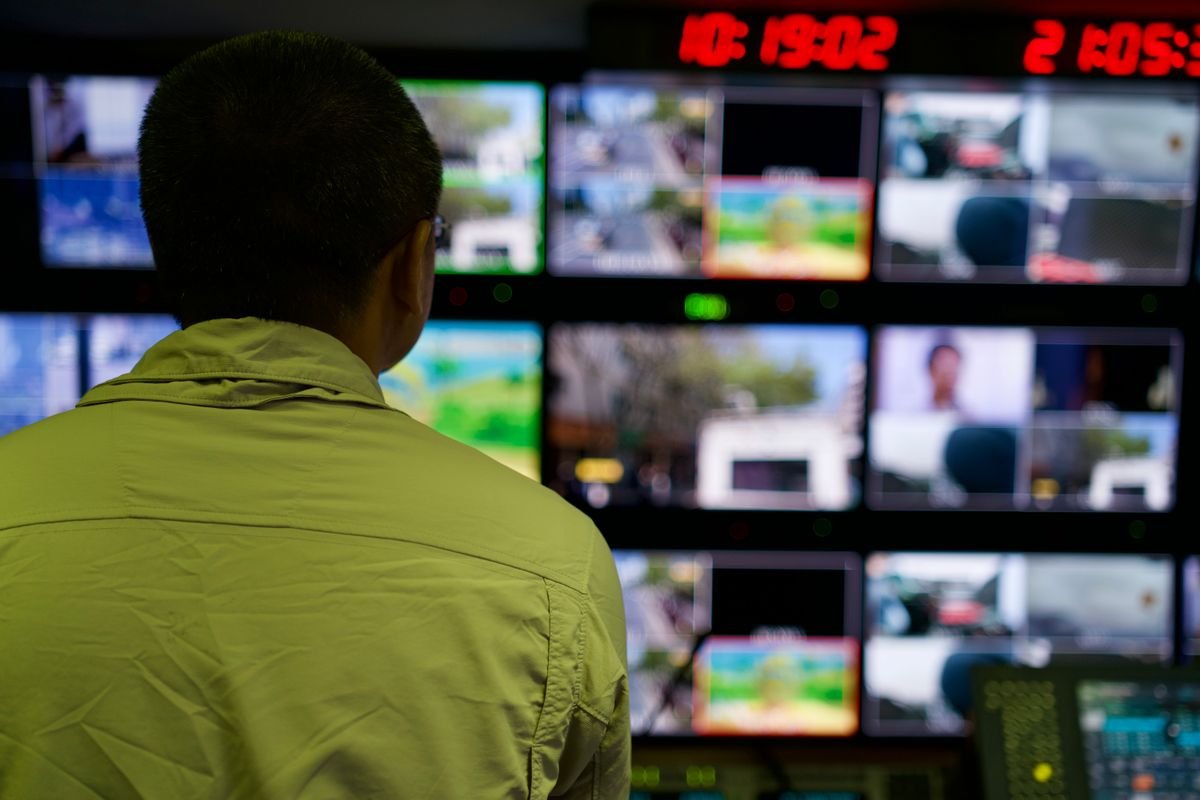 Person monitoring multiple security camera feeds on screens